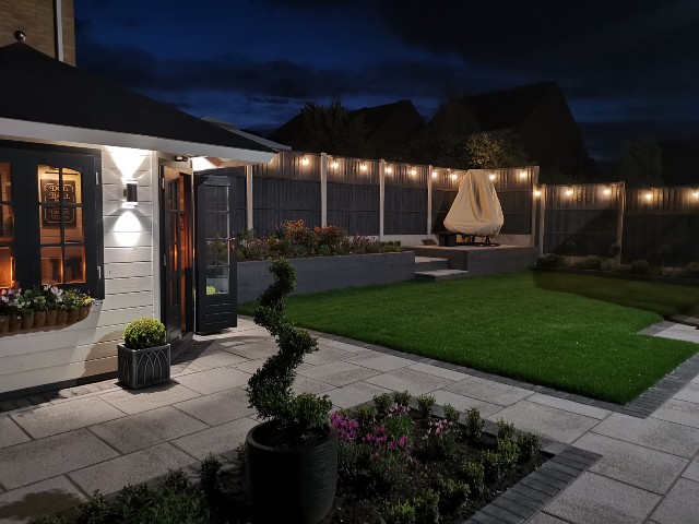 outdoor string lighting around the fence of a large garden with raised terrace