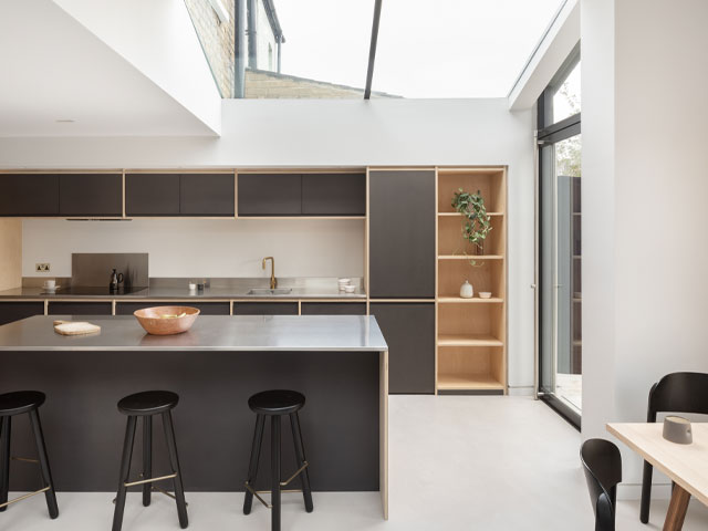 A family home with side and rear extension to make space for a contemporary kitchen with dark grey cabinets, large island, overhead glazing and pivot door to the garden