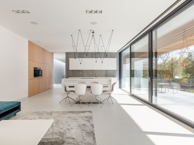 Interior of modern home with white open-plan minimalist kitchen and dining area and sliding triple-glazed doors