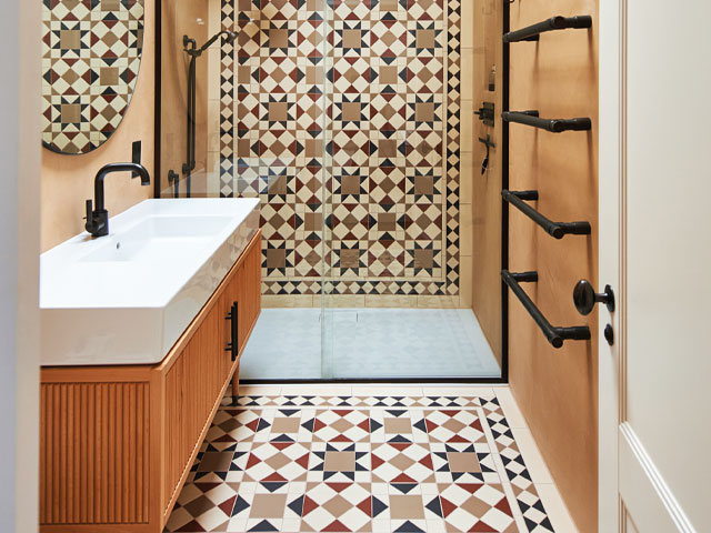 Bathroom floor ideas matching ornate tiled shower and flooring wooden sink unit with black mixer tap back towel rails